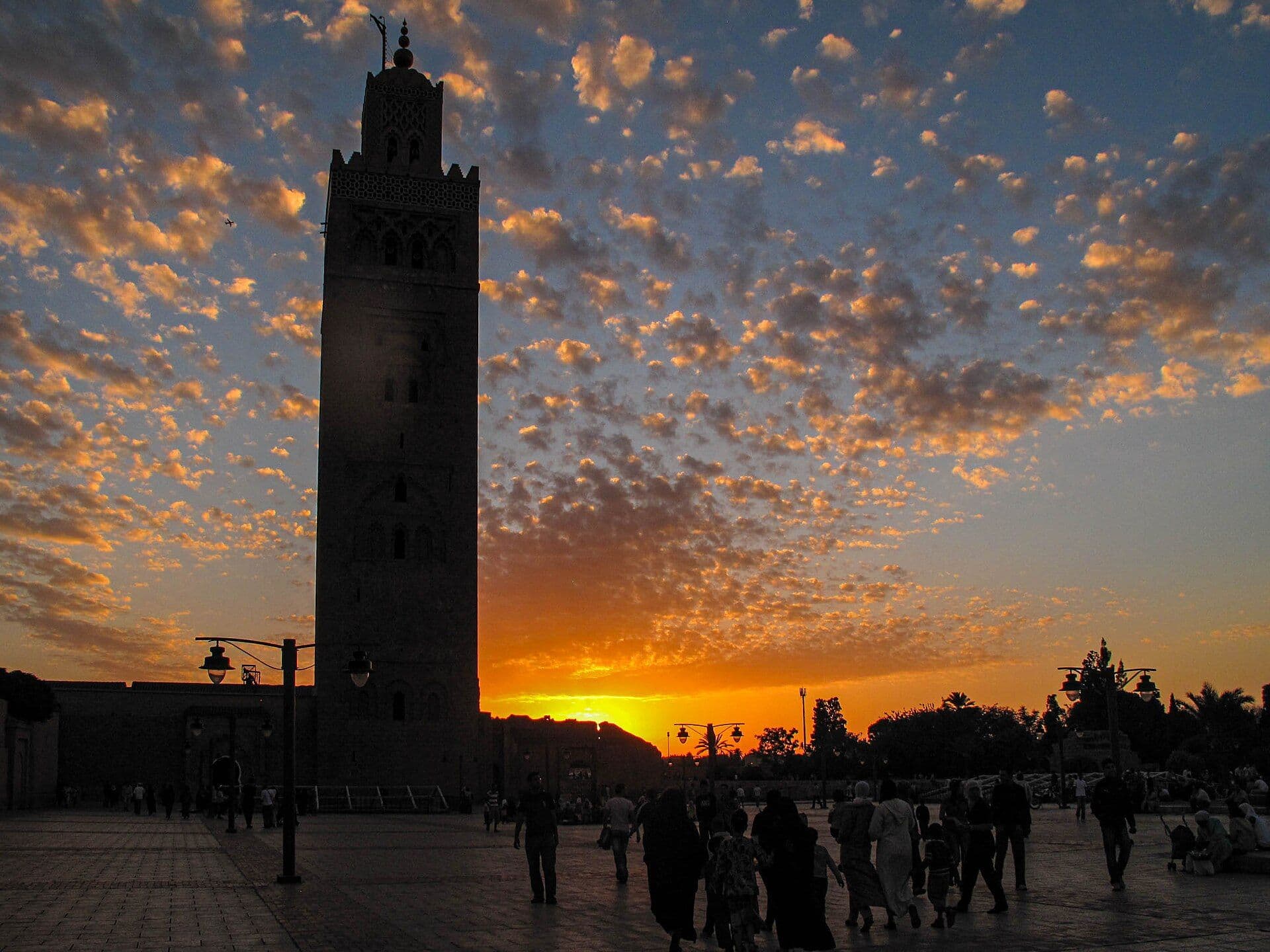 De Koutoubia-minaret in Marrakesh bij zonsondergang, met wandelaars op het plein ervoor