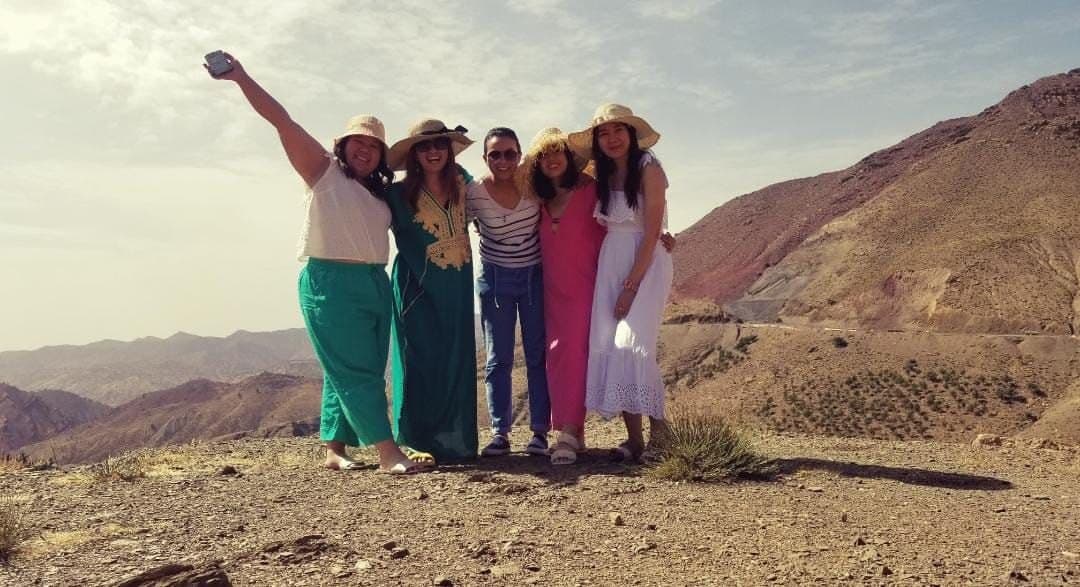 Vijf vrouwen met zonnehoeden poseren samen op een bergrug in de Atlas
